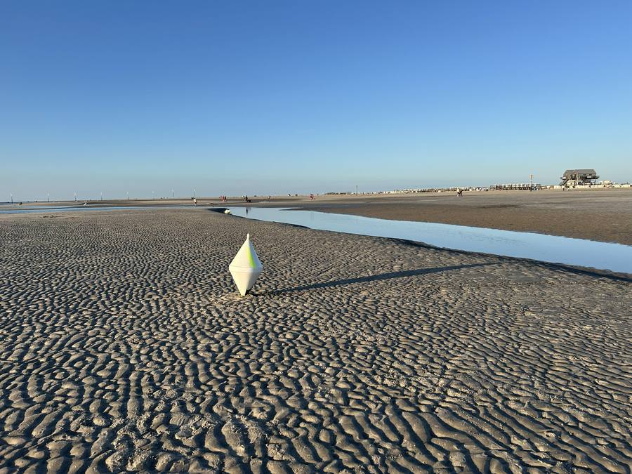 Eine Boje steht fest im Rippelsand des Watts